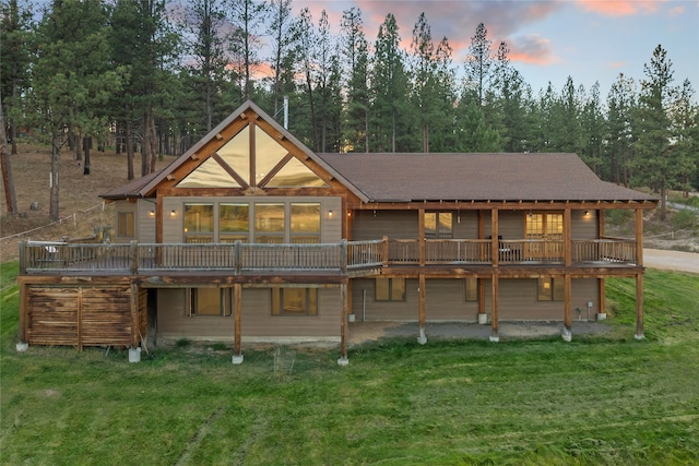 back house at dusk featuring a wooden deck and a yard