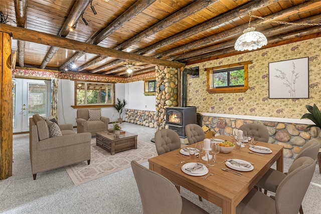 carpeted dining room featuring beamed ceiling, wooden ceiling, a wood stove, and a healthy amount of sunlight