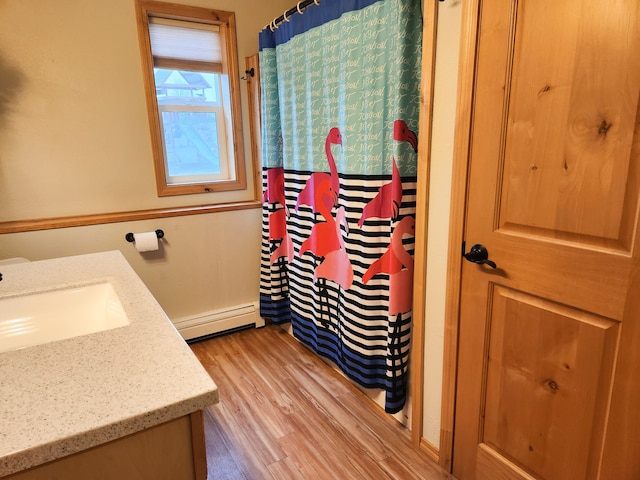 bathroom with a shower with curtain, baseboard heating, hardwood / wood-style flooring, and vanity