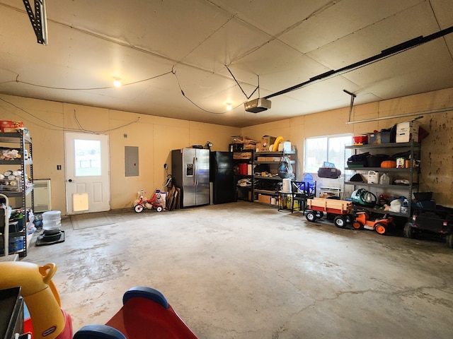 garage featuring black fridge, stainless steel refrigerator with ice dispenser, a garage door opener, and electric panel