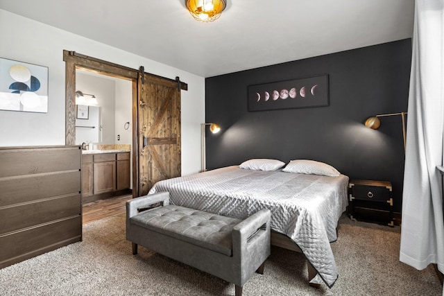 carpeted bedroom featuring a barn door, ensuite bathroom, and a sink