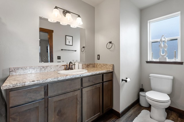 half bath with baseboards, wood finished floors, vanity, and toilet