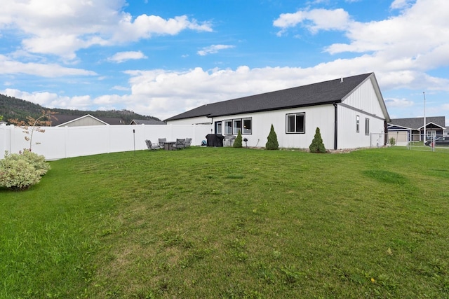 rear view of property featuring a fenced backyard, roof with shingles, and a yard
