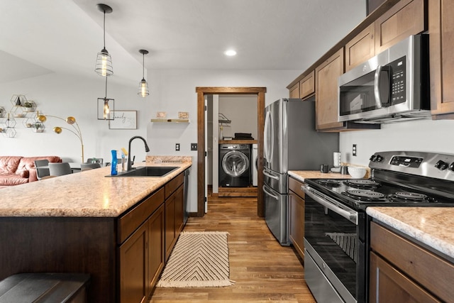 kitchen featuring stainless steel appliances, a sink, light wood-type flooring, pendant lighting, and washer / clothes dryer