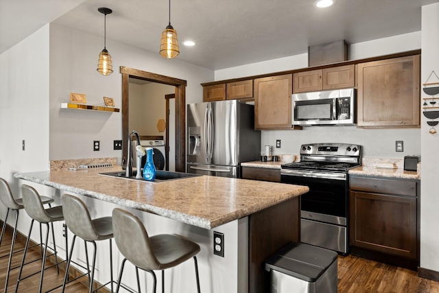kitchen featuring a sink, a breakfast bar area, stainless steel appliances, dark wood finished floors, and a peninsula