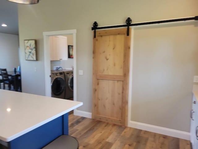 interior space with washer and clothes dryer, light wood-type flooring, a barn door, and blue cabinetry