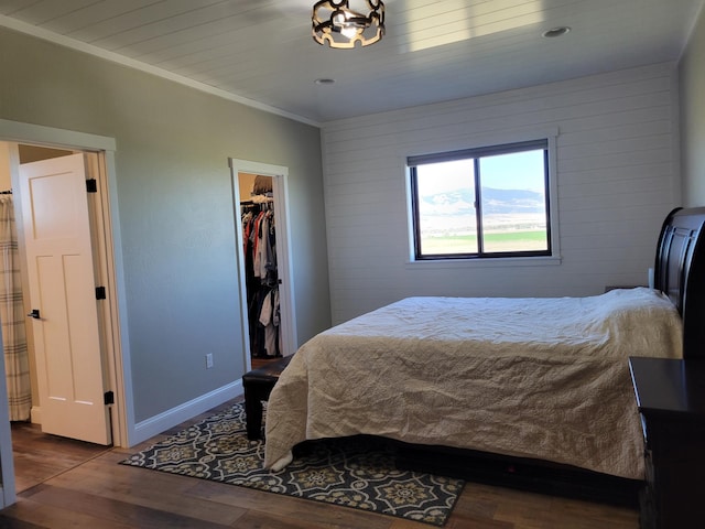 bedroom with wood walls, a closet, a spacious closet, crown molding, and hardwood / wood-style floors