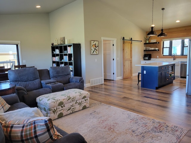 living room featuring a barn door, light hardwood / wood-style flooring, and high vaulted ceiling