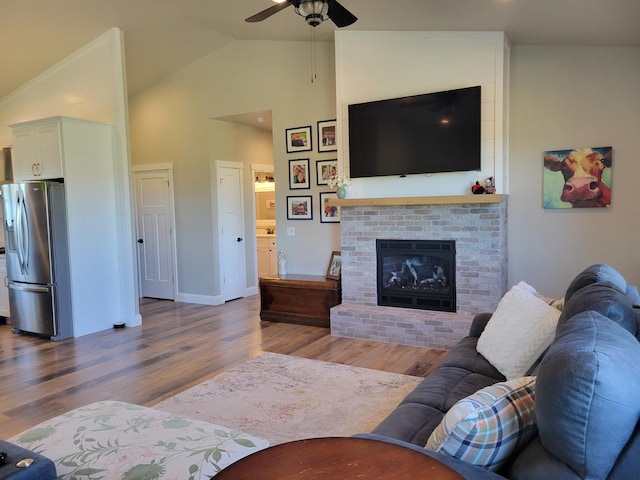 living room featuring ceiling fan, lofted ceiling, a brick fireplace, and wood-type flooring