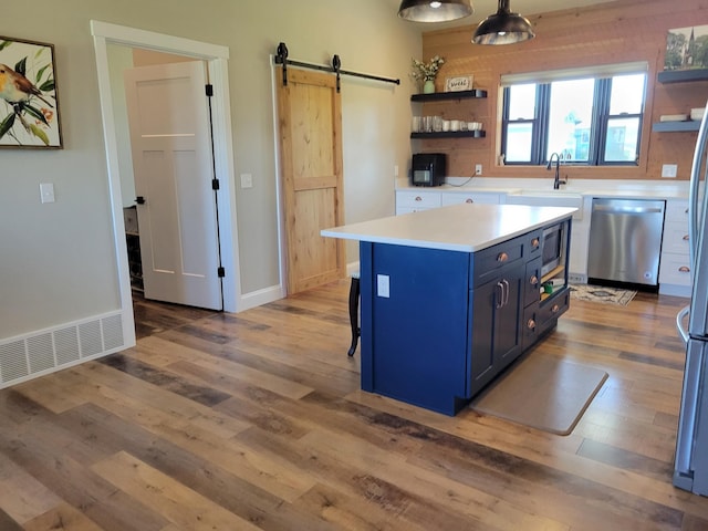 kitchen featuring blue cabinetry, appliances with stainless steel finishes, hardwood / wood-style floors, and a barn door