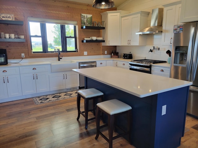 kitchen featuring a kitchen island, wall chimney range hood, white cabinetry, stainless steel appliances, and a kitchen bar