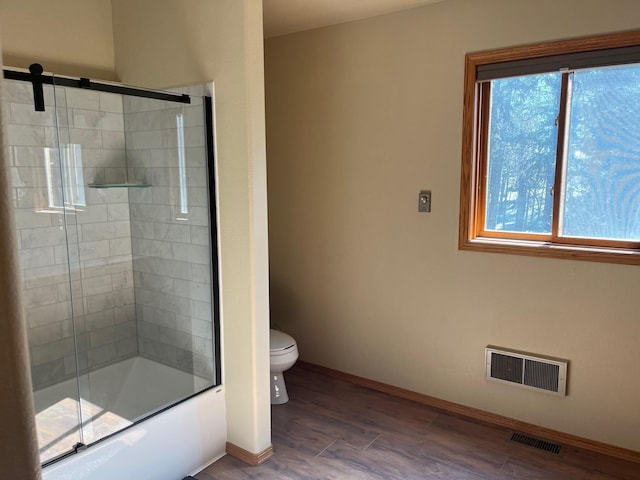 bathroom with hardwood / wood-style flooring, a healthy amount of sunlight, toilet, and shower / bath combination with glass door