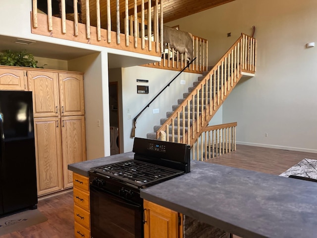 kitchen with dark hardwood / wood-style floors, washer / dryer, light brown cabinetry, and black appliances