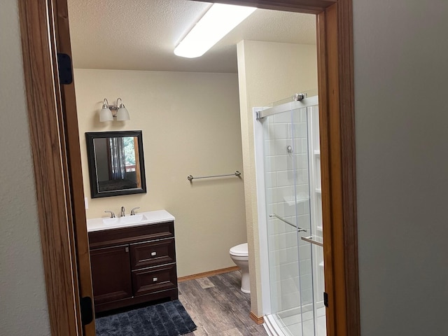 bathroom featuring wood-type flooring, vanity, toilet, a shower with door, and a textured ceiling