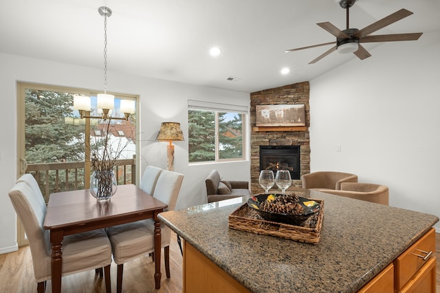 dining room with light hardwood / wood-style floors, ceiling fan with notable chandelier, a fireplace, and lofted ceiling