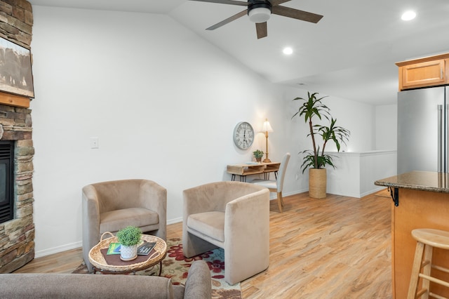 living room with light wood-type flooring, a fireplace, vaulted ceiling, and ceiling fan