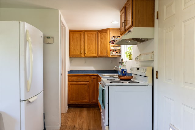 kitchen featuring white appliances, light wood-style floors, brown cabinets, under cabinet range hood, and a sink