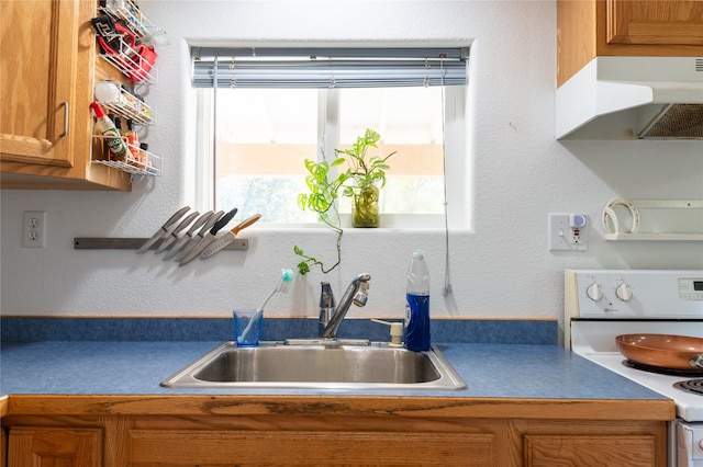 kitchen with under cabinet range hood, electric stove, brown cabinets, and a sink