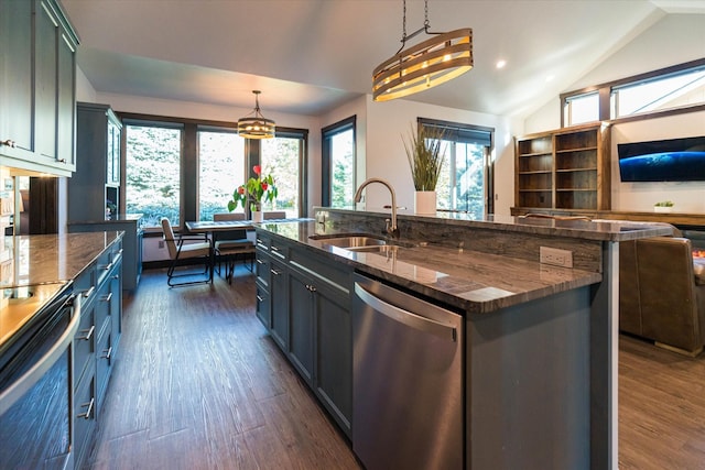 kitchen featuring an island with sink, stainless steel appliances, sink, dark stone counters, and pendant lighting