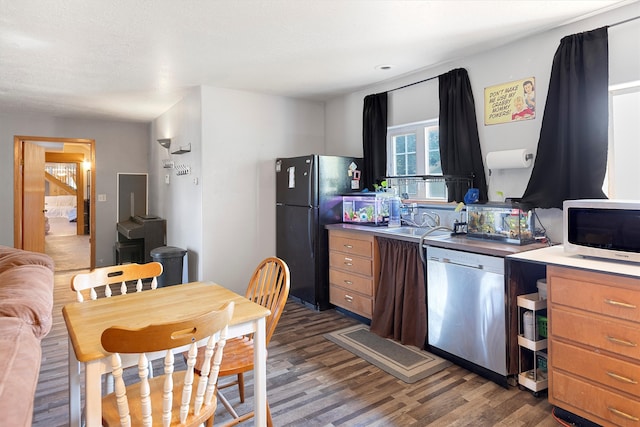 kitchen with sink, dark wood-type flooring, black refrigerator, and stainless steel dishwasher