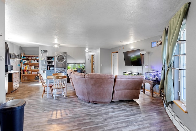 living room featuring a textured ceiling, light hardwood / wood-style flooring, stacked washer / drying machine, and a baseboard heating unit