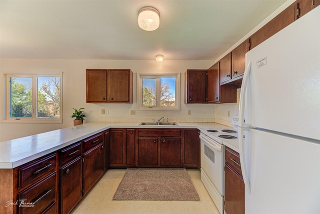 kitchen featuring a peninsula, light countertops, white appliances, and a sink