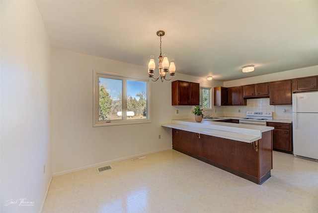 kitchen with hanging light fixtures, plenty of natural light, kitchen peninsula, and white appliances