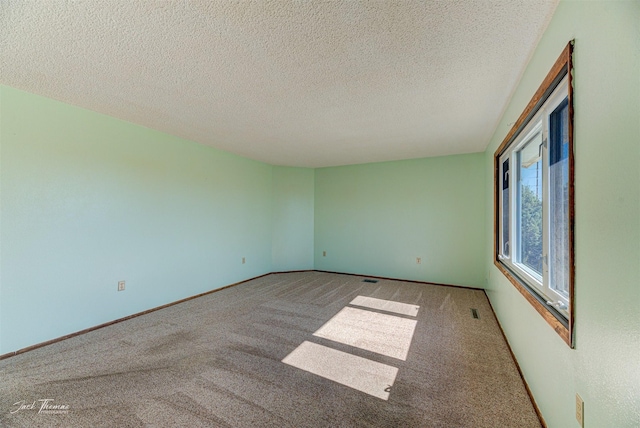 unfurnished room with carpet floors, a textured ceiling, baseboards, and visible vents