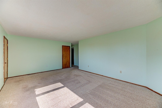 spare room with a textured ceiling, baseboards, and light carpet
