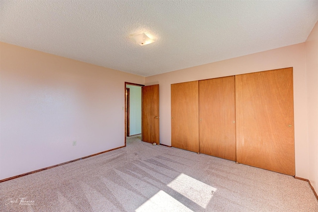 unfurnished bedroom with a textured ceiling, a closet, baseboards, and light carpet