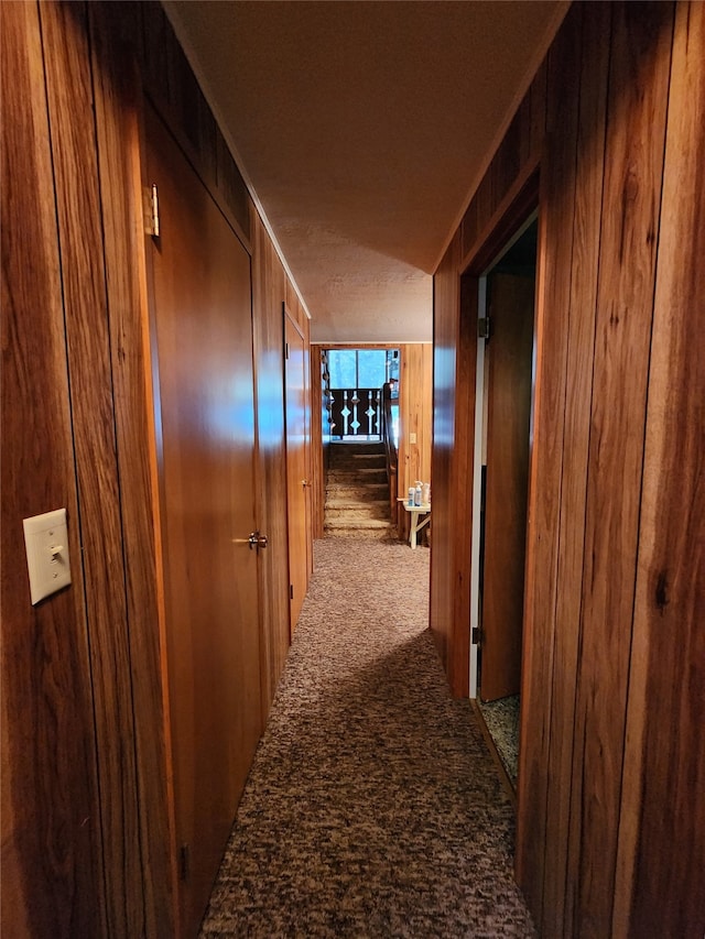 hall with wood walls, a textured ceiling, and light colored carpet