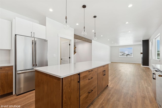 kitchen with white cabinets, a center island, hanging light fixtures, light hardwood / wood-style flooring, and high end fridge