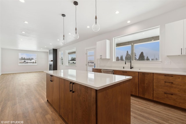 kitchen with white cabinets, a kitchen island, light hardwood / wood-style floors, sink, and hanging light fixtures