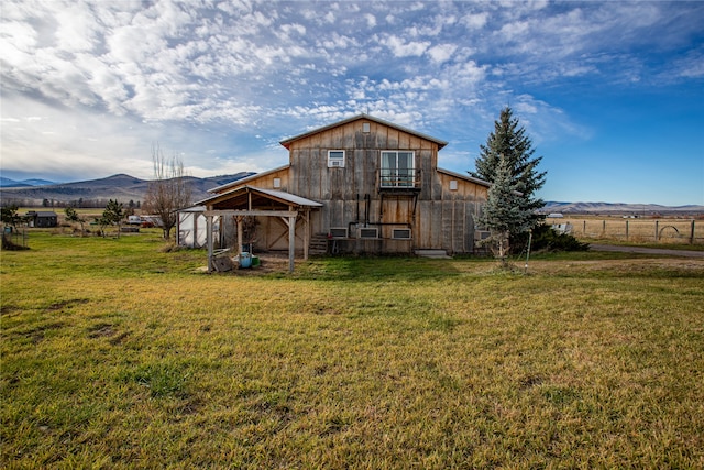 back of property with a yard, an outdoor structure, a mountain view, and a rural view