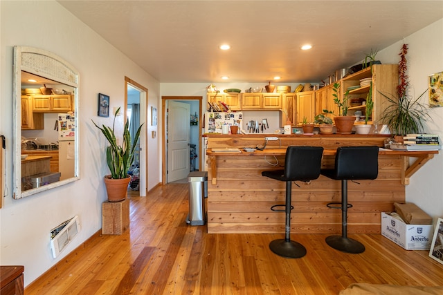 kitchen featuring light hardwood / wood-style flooring, fridge, a kitchen breakfast bar, heating unit, and light brown cabinets