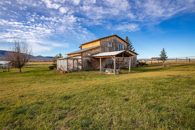 back of property featuring a rural view, a mountain view, a yard, and an outbuilding