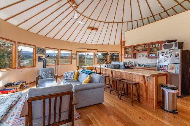 living room with ceiling fan, high vaulted ceiling, a wood stove, and light wood-type flooring