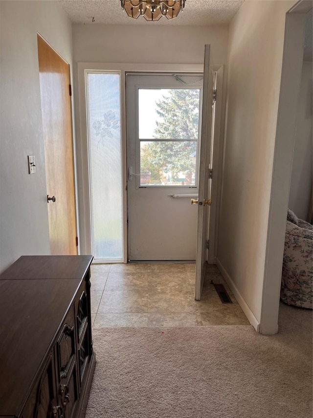 doorway with a chandelier, visible vents, a textured ceiling, and light carpet