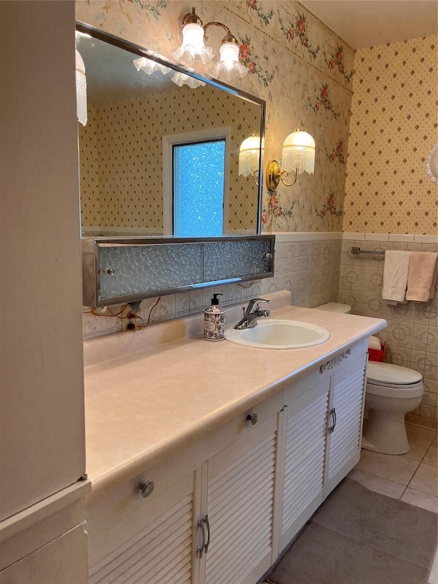 bathroom featuring toilet, a wainscoted wall, vanity, wallpapered walls, and tile patterned floors