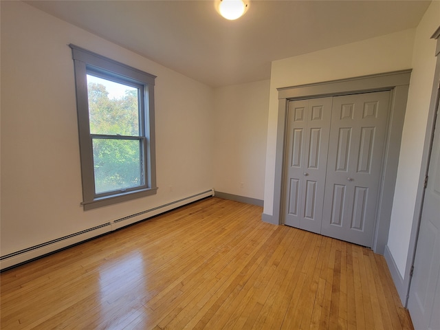 unfurnished bedroom with a baseboard radiator, light wood-type flooring, and a closet