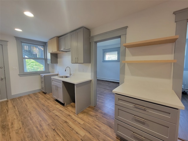 kitchen with gray cabinets, light wood-type flooring, sink, and a baseboard heating unit