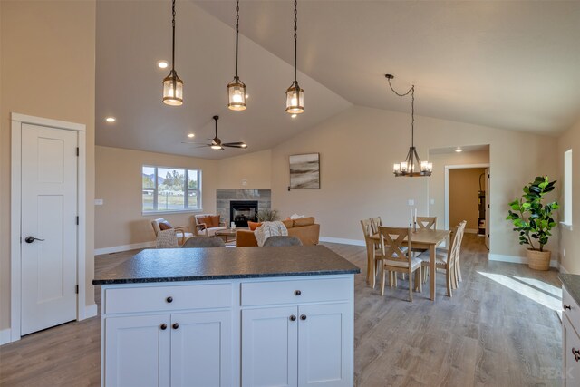 kitchen with light wood-type flooring, a fireplace, hanging light fixtures, vaulted ceiling, and white cabinets