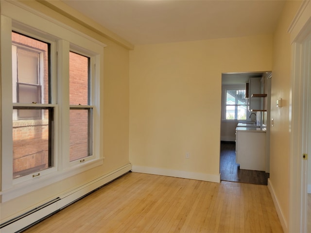 empty room with a baseboard radiator, light wood-type flooring, and sink