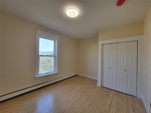 unfurnished bedroom with a closet, a baseboard heating unit, and light hardwood / wood-style flooring