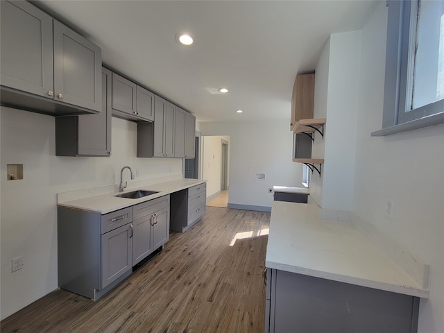 kitchen with light stone counters, stove, sink, gray cabinets, and light hardwood / wood-style floors