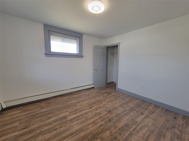 unfurnished bedroom with dark hardwood / wood-style flooring, a walk in closet, a closet, and a baseboard radiator