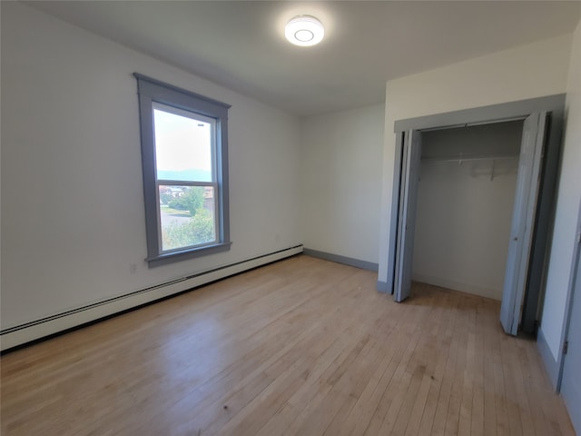 unfurnished bedroom featuring a baseboard radiator, light hardwood / wood-style flooring, and a closet