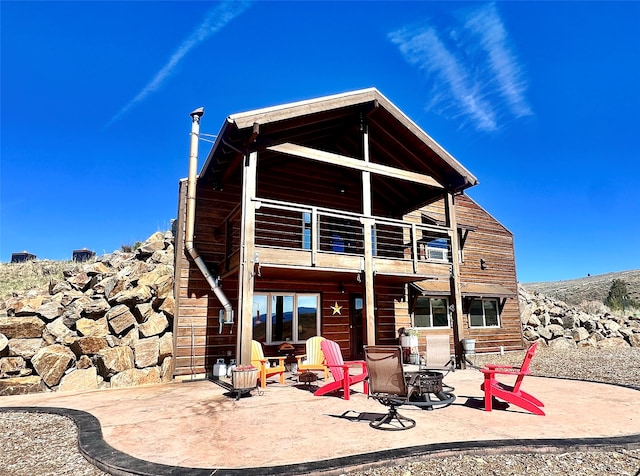 rear view of house featuring a balcony, a patio, and an outdoor fire pit