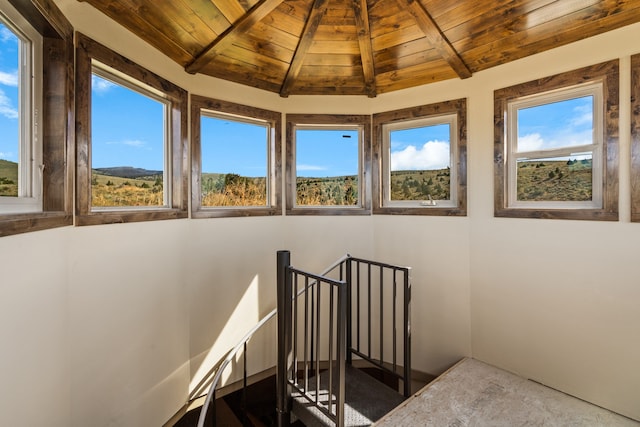 stairway featuring lofted ceiling with beams, wooden ceiling, and a healthy amount of sunlight