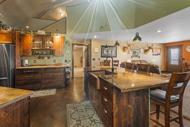 kitchen with an island with sink, sink, decorative light fixtures, and stainless steel refrigerator